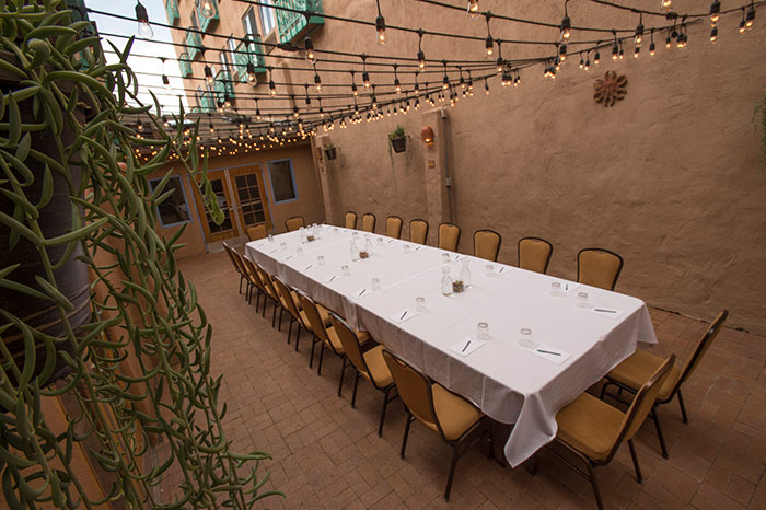 A long table set for dining in an outdoor courtyard with string lights and plants.