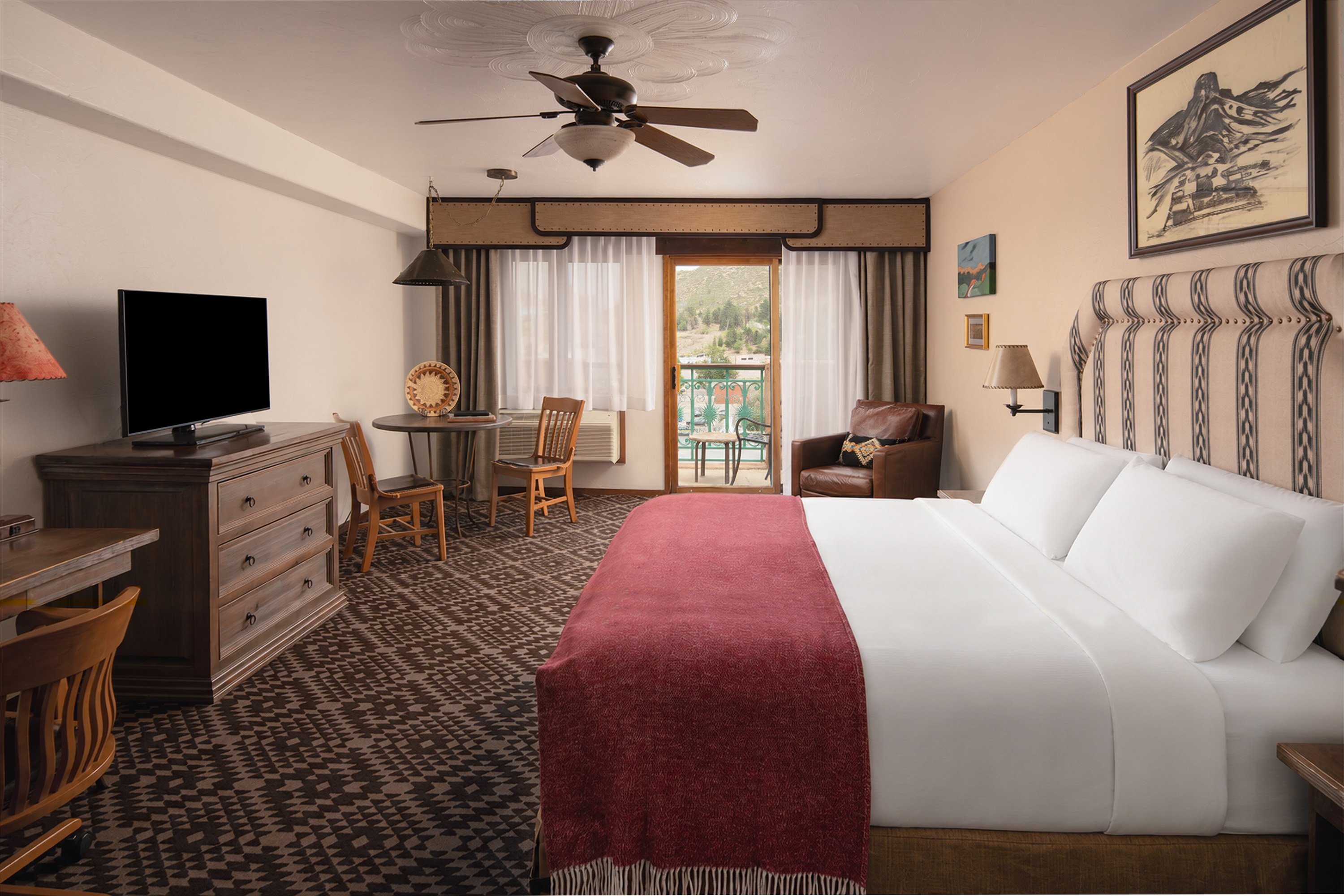 A wide hotel room with a large bed, desk, TV, and balcony