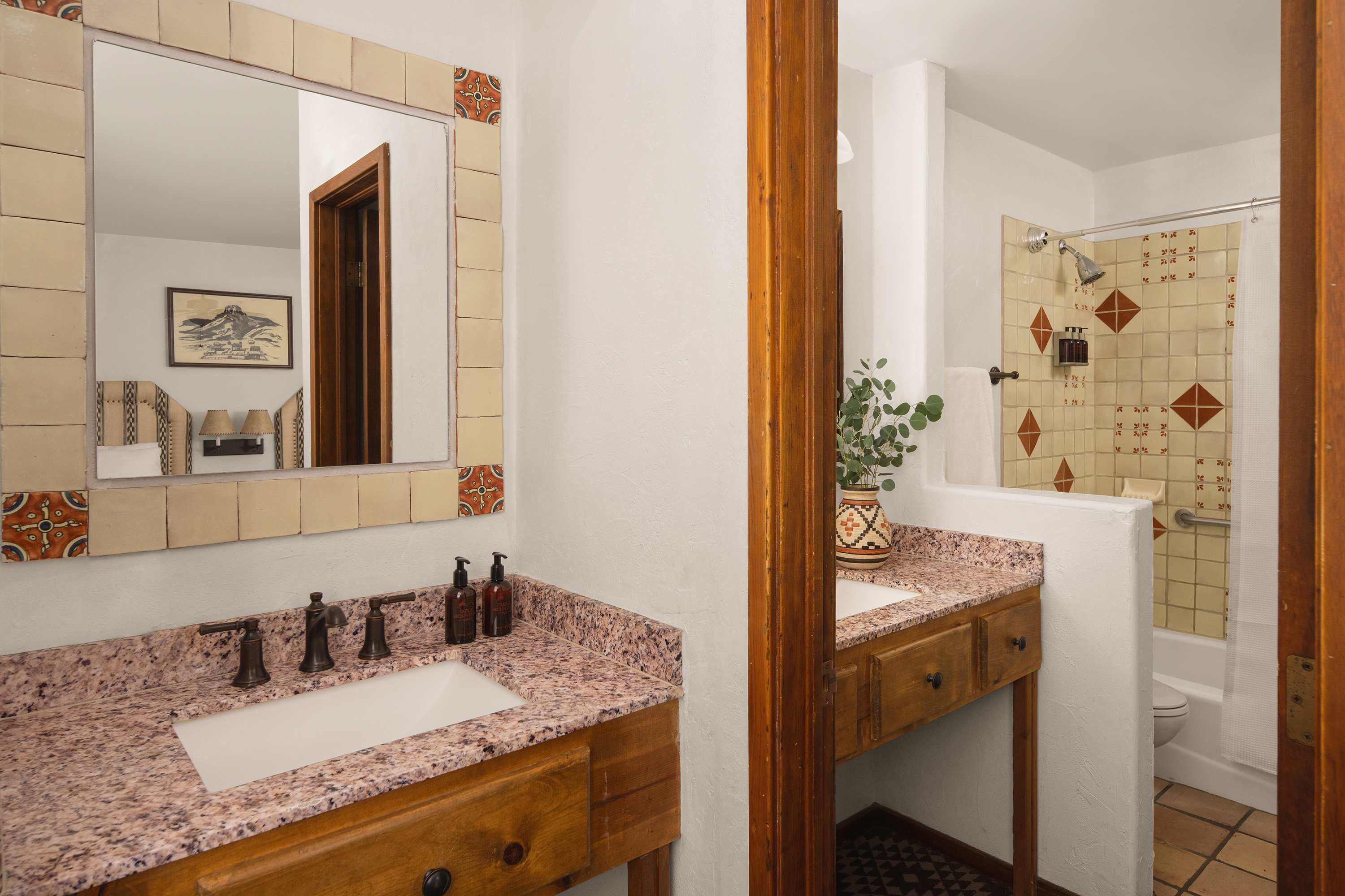 A bathroom with a double vanity, granite countertops, and a shower