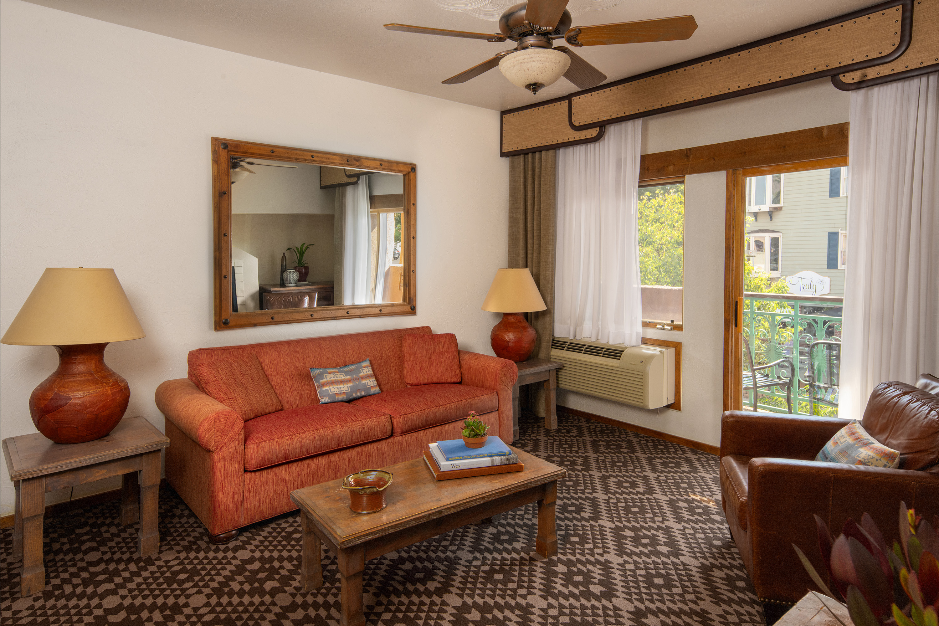 A wide view of a hotel room's living area with a sofa, coffee table, armchair, and balcony