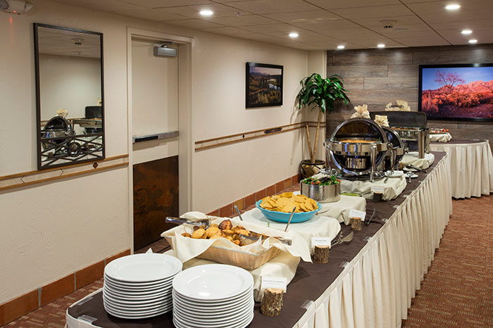 A buffet table with food and plates in a dining area with beige walls and brown carpet.