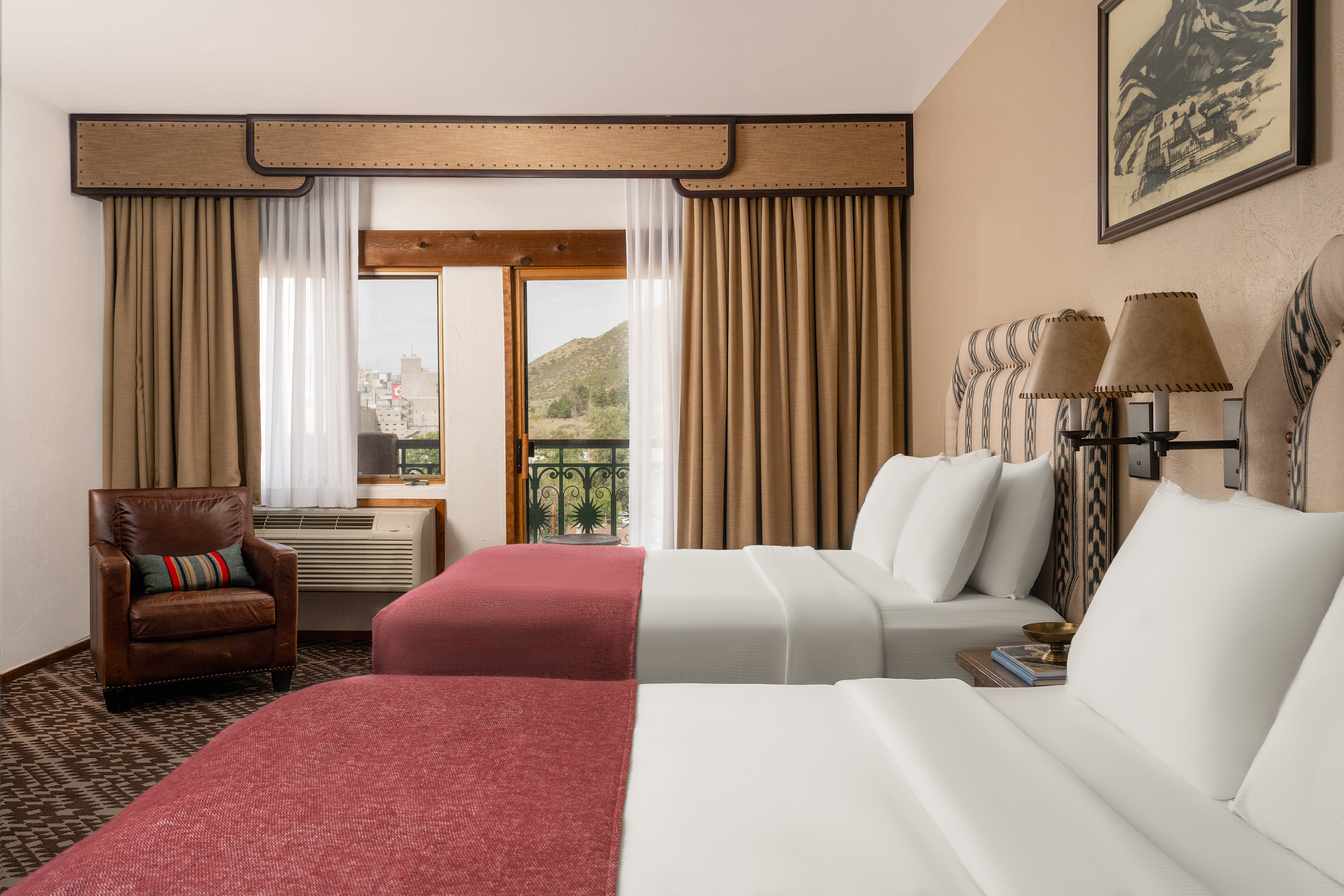 A hotel room with two beds, a window with a view, and a brown armchair.