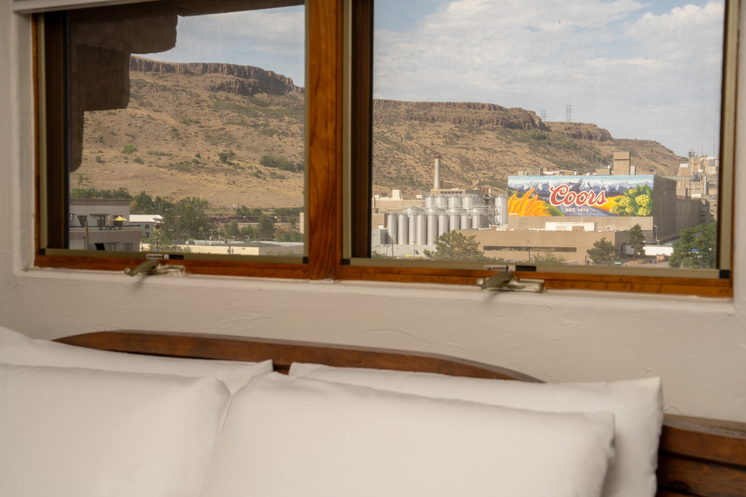 A hotel room with a bed and a window showing a view of a mountain and a Coors brewery.