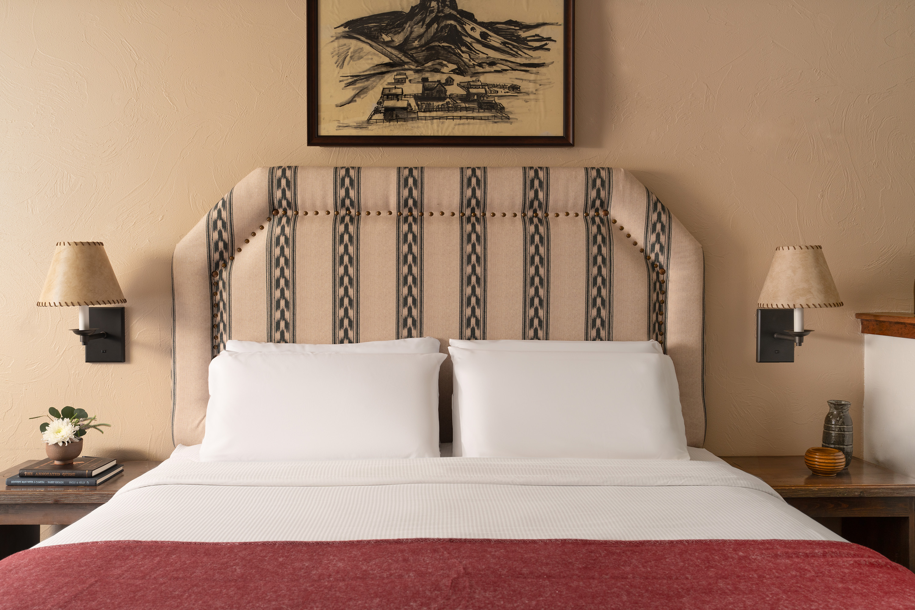 A neatly made bed with a large, upholstered headboard, flanked by nightstands with lamps and a piece of artwork above.