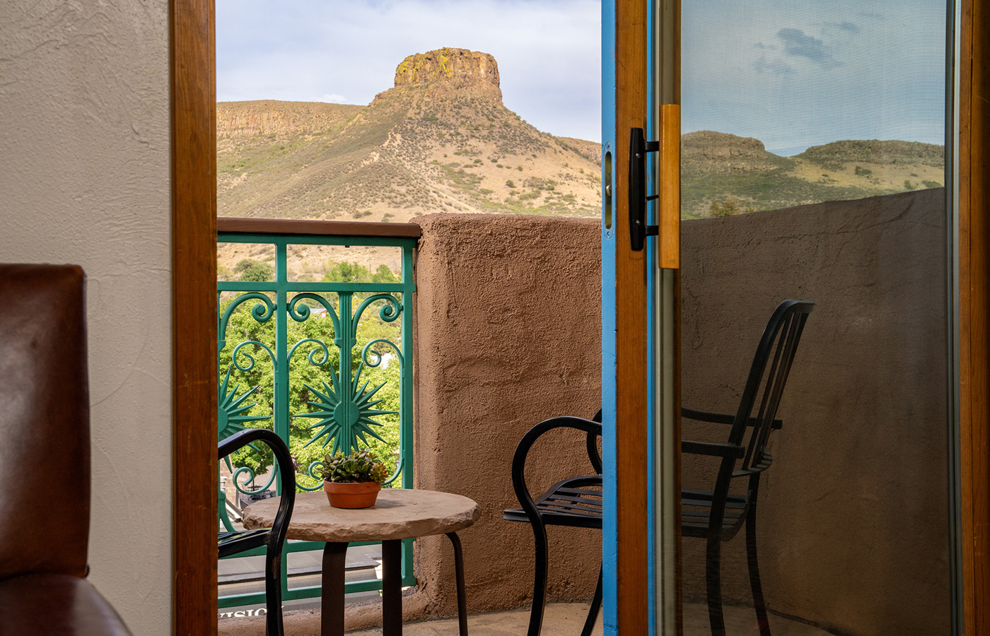 A balcony with a table, chairs, and a potted plant overlooking a mountain view.